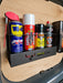 A black shelf, designed as an Aerosol Can Holder, holds five cans: WD-40, Gorilla Filler, CRC Silicone Spray, Wynn's Brake and Parts Cleaner, and another cleaner. Its wall-mounted design is ideal for van & workshop storage against a wooden surface.