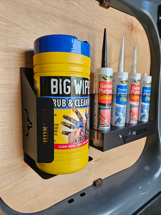 A wall-mounted organizer with a sleek design holds a container of cleaning wipes and four tubes of silicone sealant. The Wipe Dispenser Holder label reads "BIG WIPES," and the backdrop features a wooden panel, ensuring a universal fit for any setting.